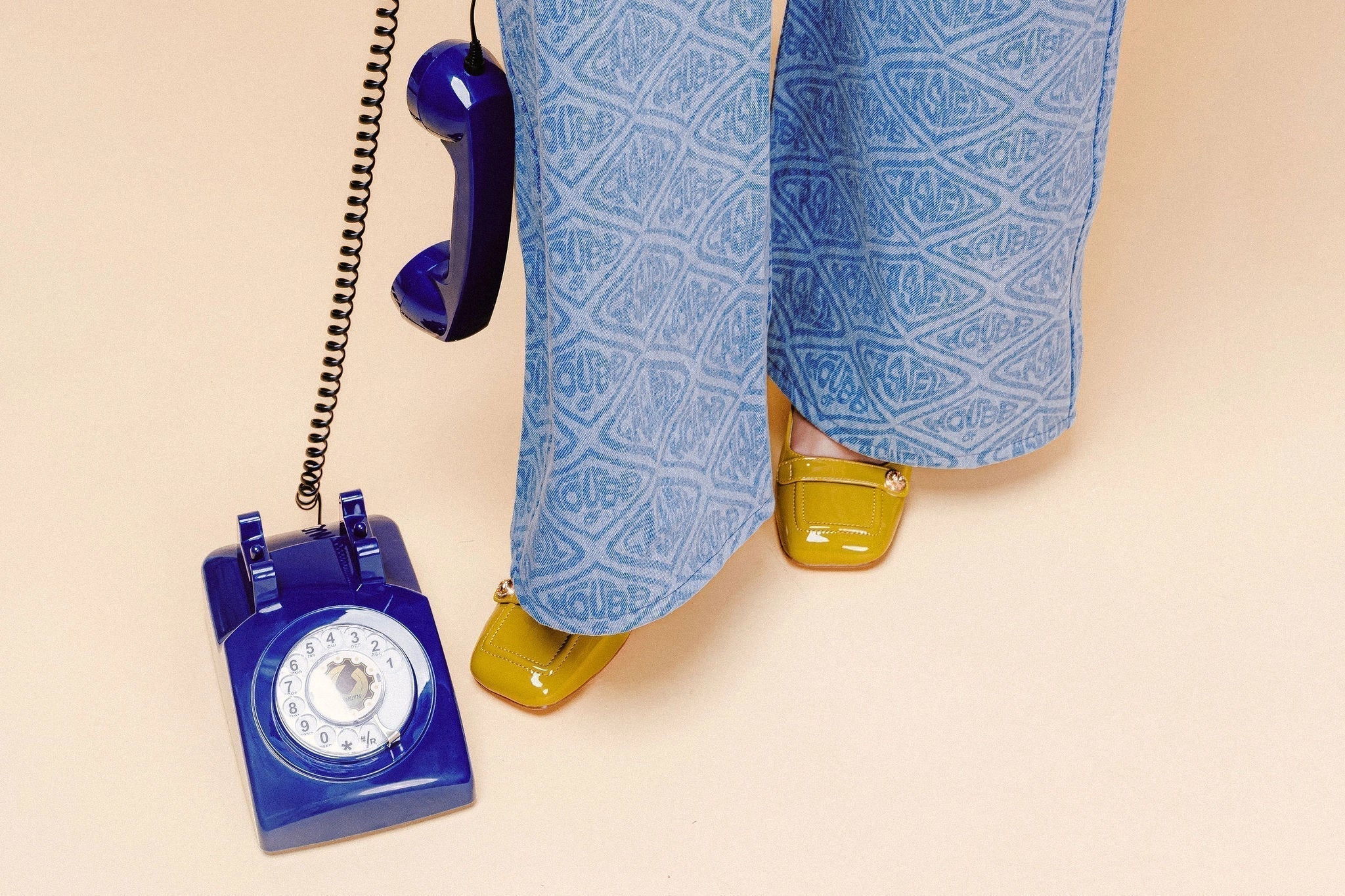 A close up of printed yellow jeans and yellow patent leather shoes with a blue rotary phone