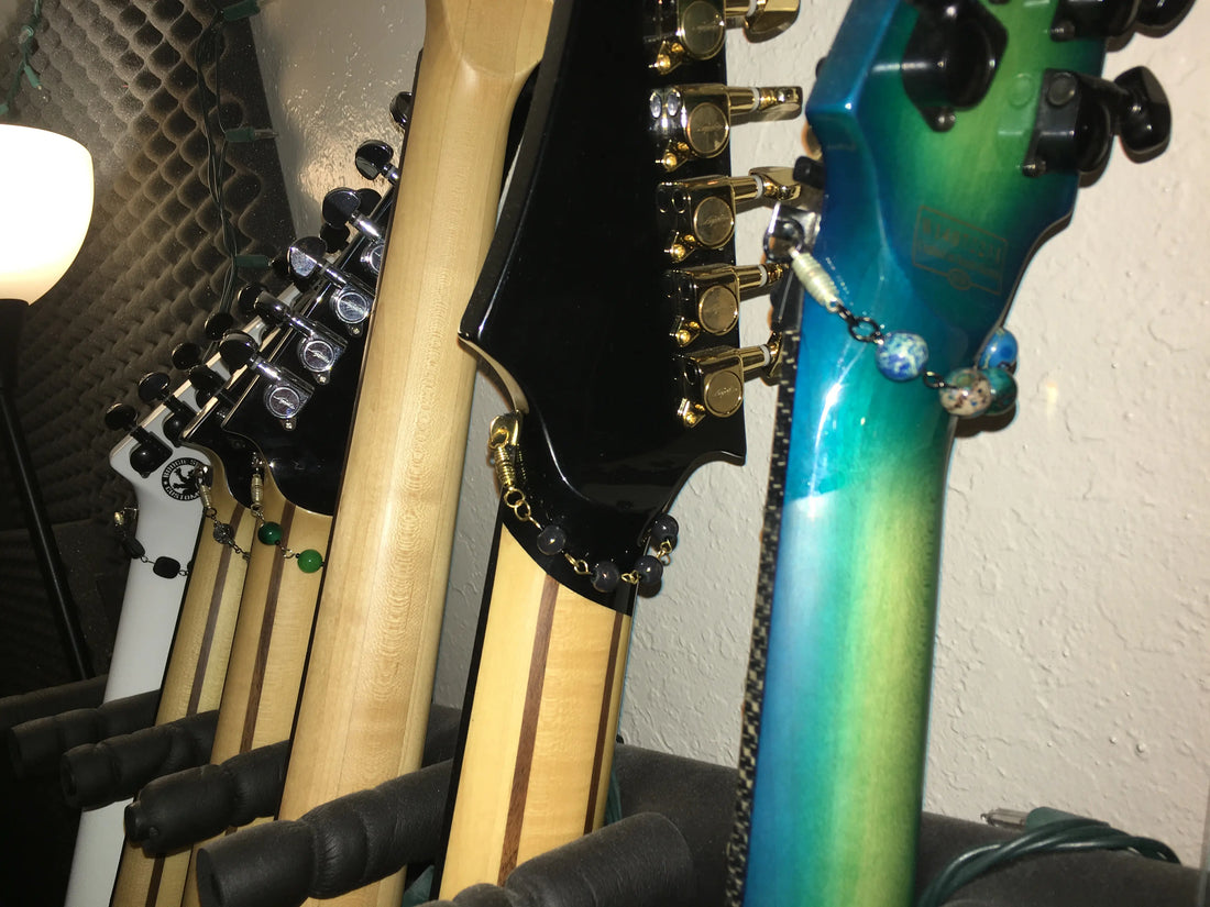 Multiple electric guitars displayed with handmade Muffle Cuffs featuring colorful beads and chains wrapped around the guitar necks.