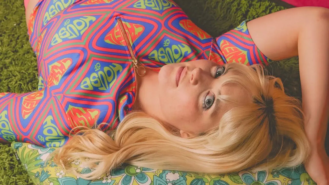 Model wearing the Sophia Mock Neck Top by House of Caswell, featuring a vibrant retro-inspired monogram print, styled with pink pants in a nostalgic, color-rich setting.